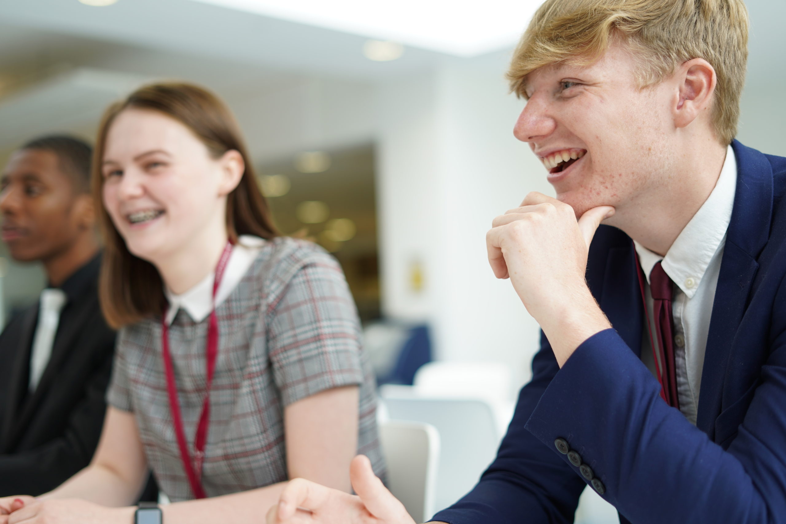Two Post-16 students are shown laughing and smiling at people across the table from them.