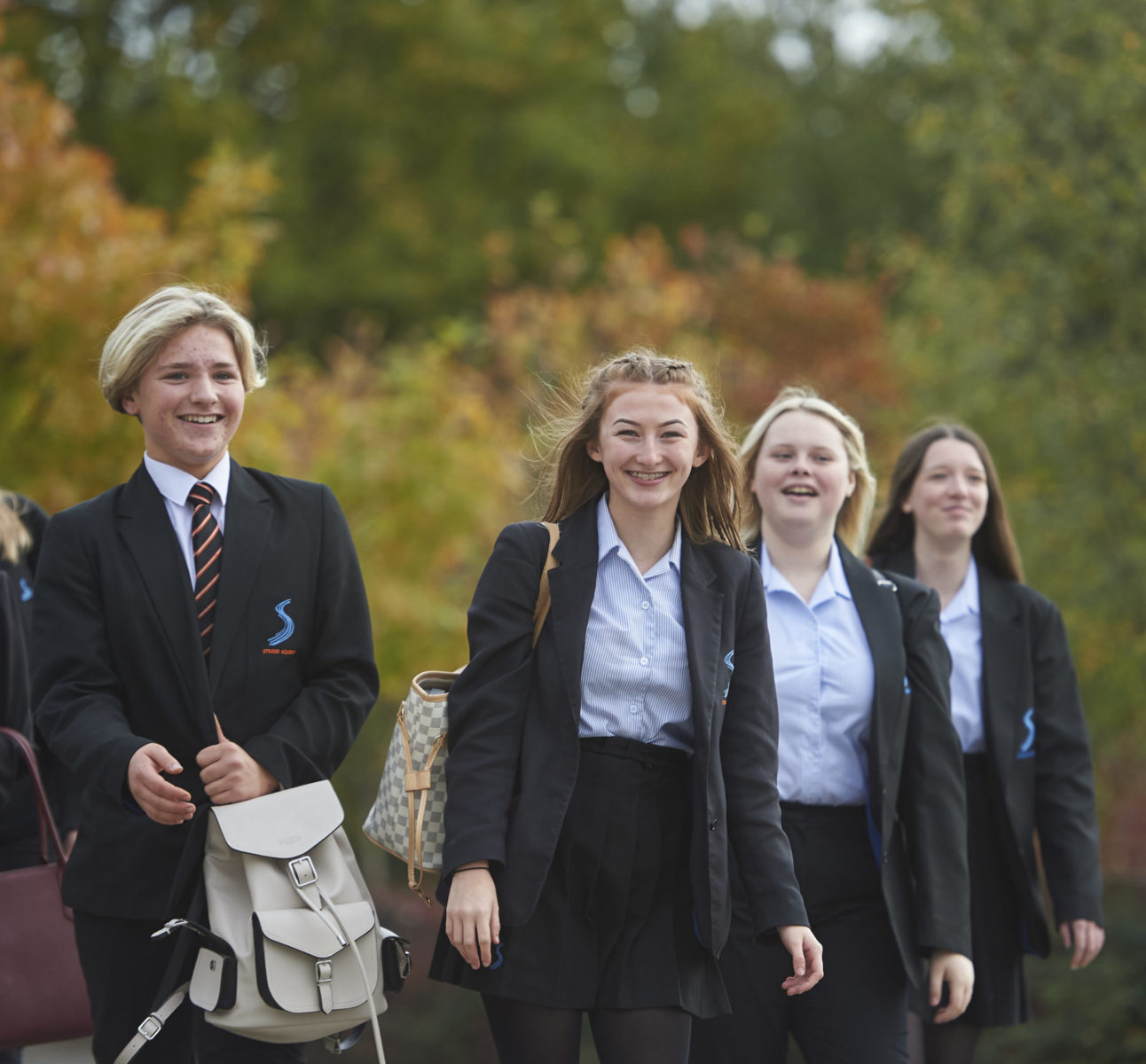 Four Strood Academy students pose outside for the camera, wearing their school bags on their backs.
