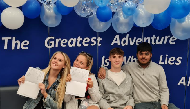 Photo of Year 11 students smiling for the camera and holding up their GCSE results sheets.