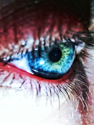 Close up of an person with blue eyes and red eyeliner on the waterline