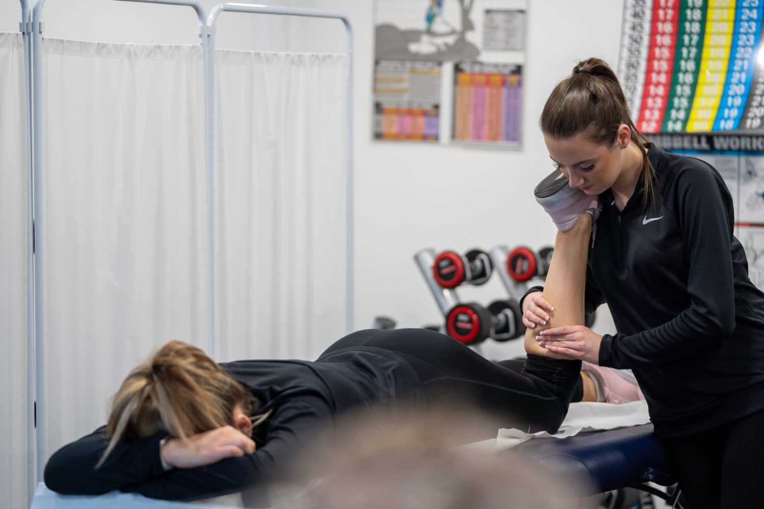 A student lying on a physio bed with another student working on their leg
