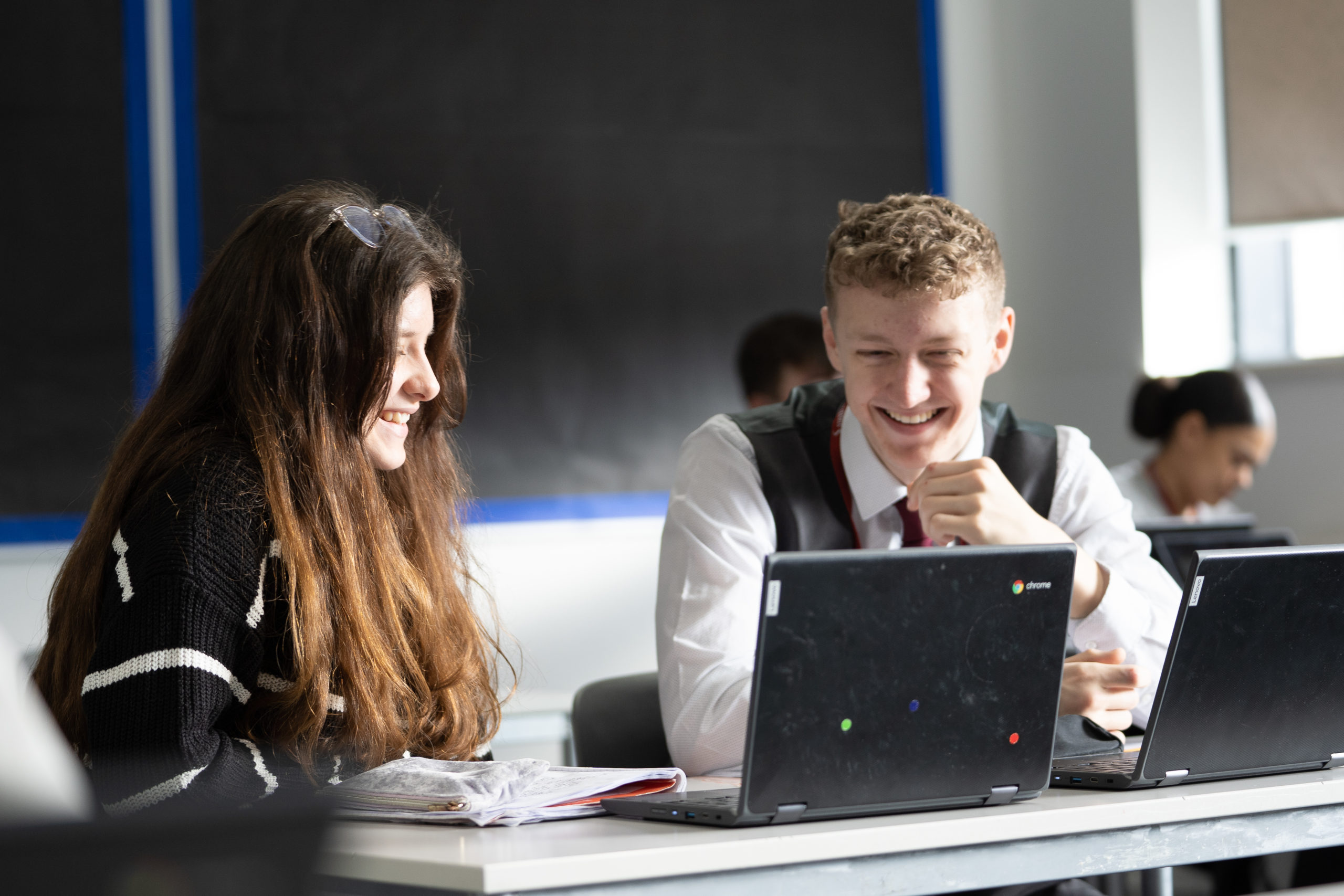 Two students smiling at a Chromebook