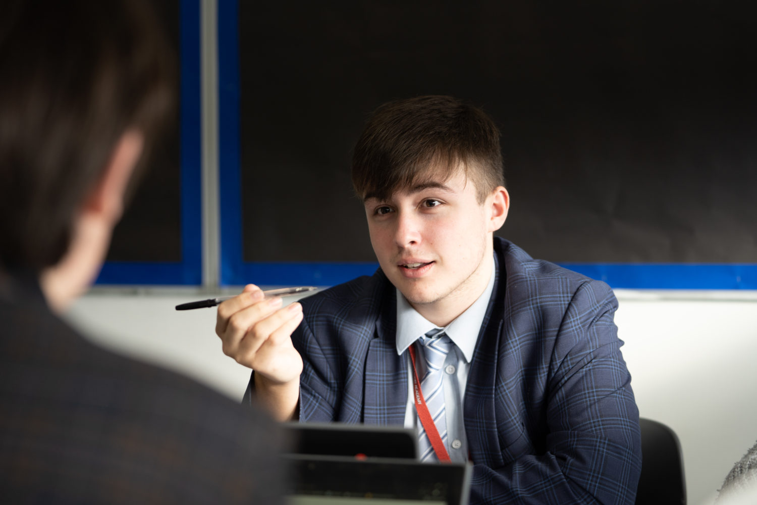 A student in a suit holding a pen talking to someone