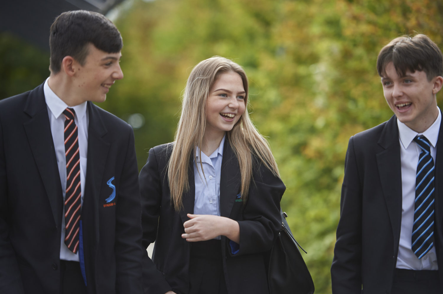 Three students talking and smiling while walking towards the camera.