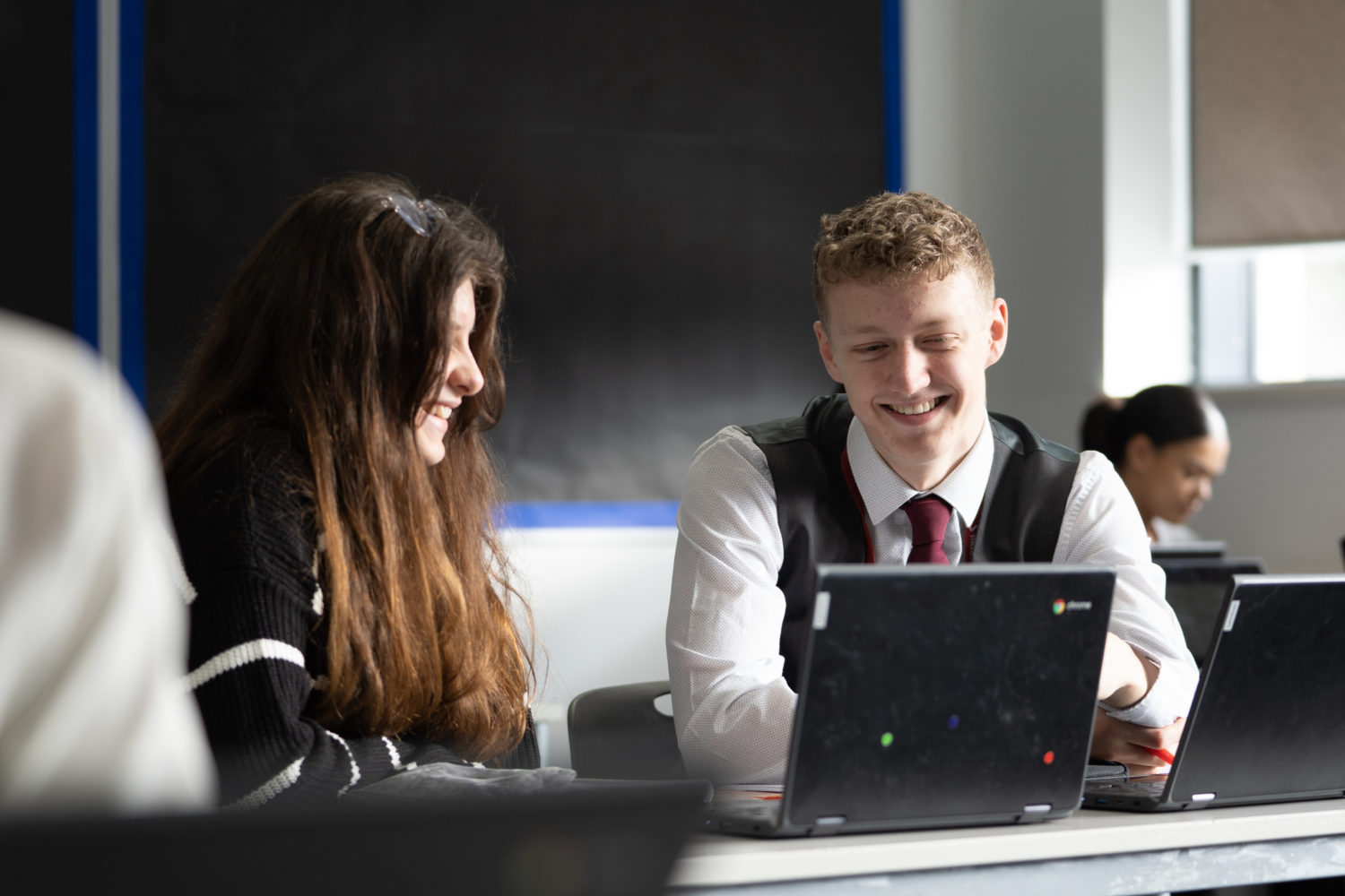 Two students smiling at a Chromebook