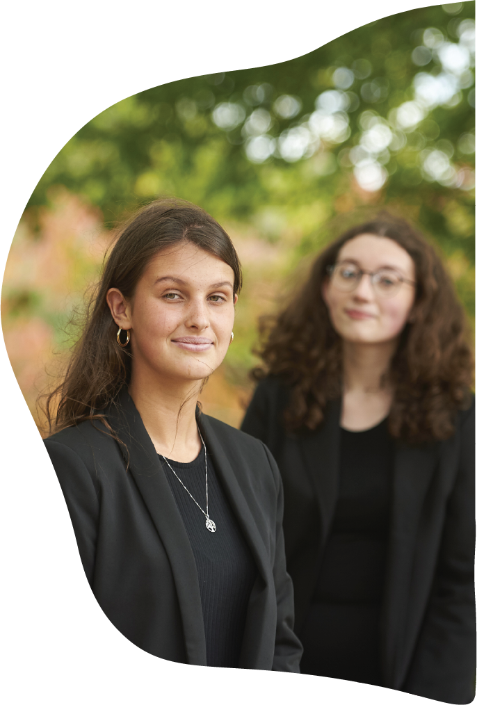 Two girls, one in the foreground and one in the background both wearing smart dress