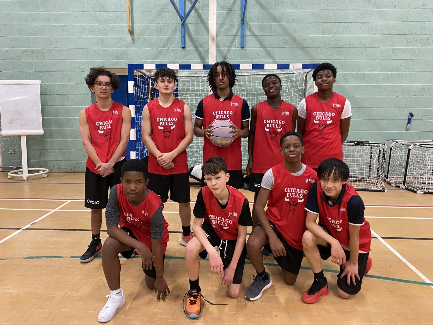 A team of students wearing basketball kits smiling for a photo