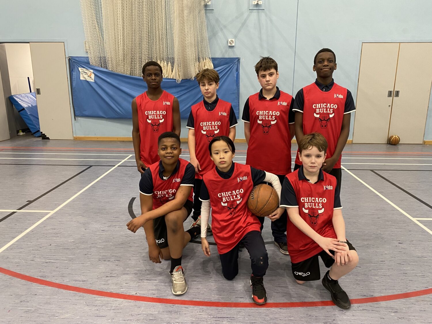 A team of students wearing basketball kits smiling for a photo